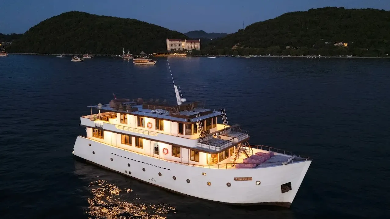 A crewed motor yacht lit up at dusk off a Flores island