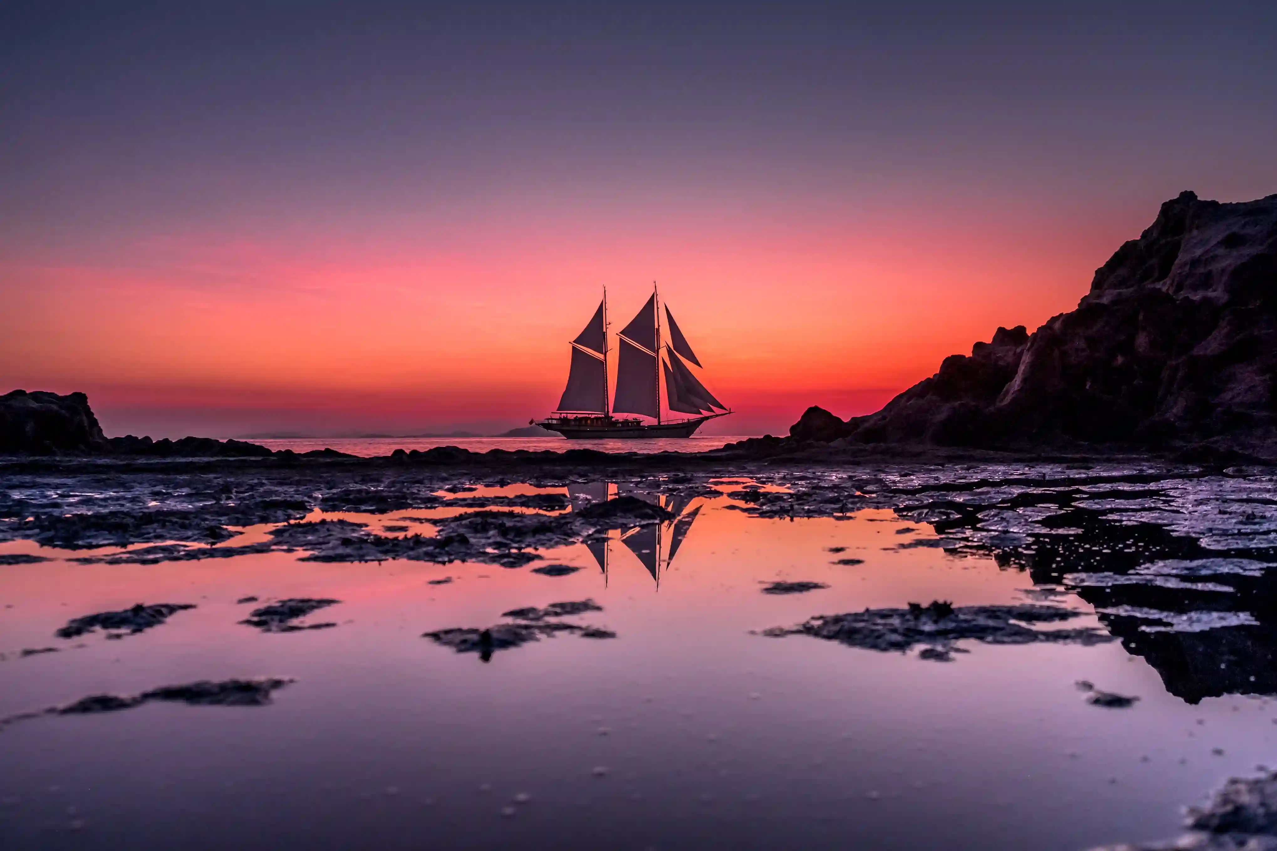 A phinisi under full sail at sunset in the Flores Sea