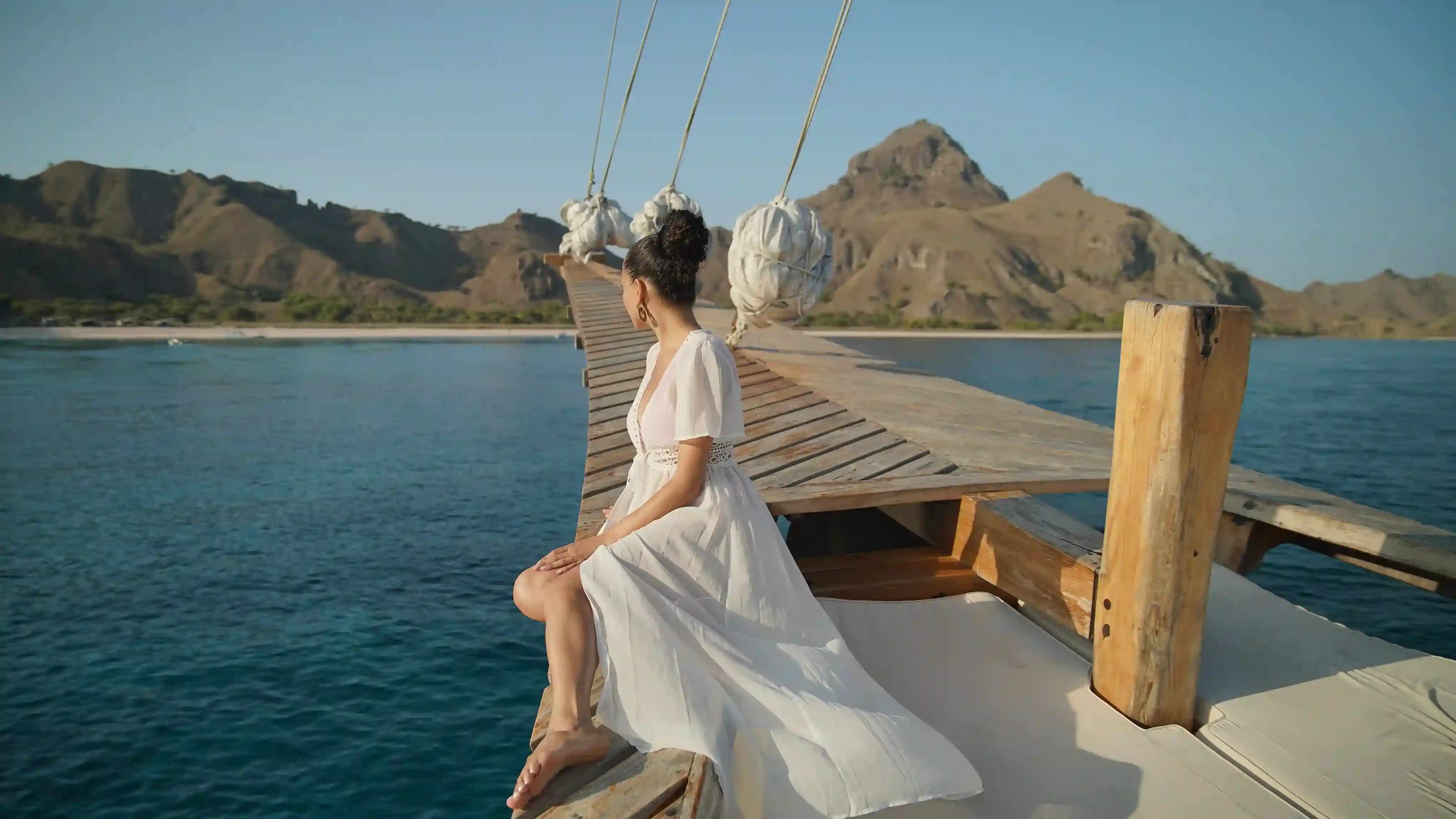 A guest on the bowsprit of a phinisi approaching the islands