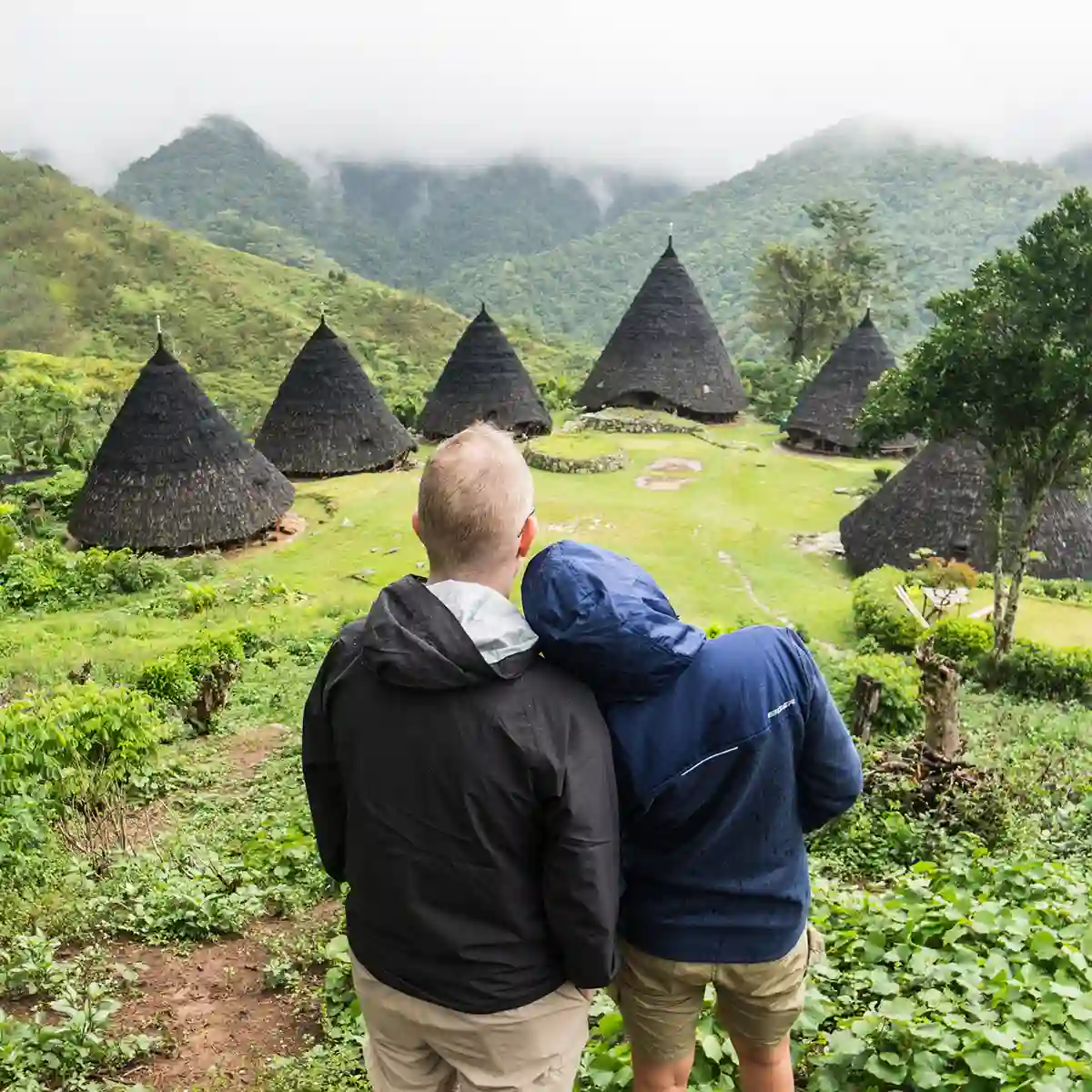 Travellers looking out over the cone-roofed houses of Wae Rebo